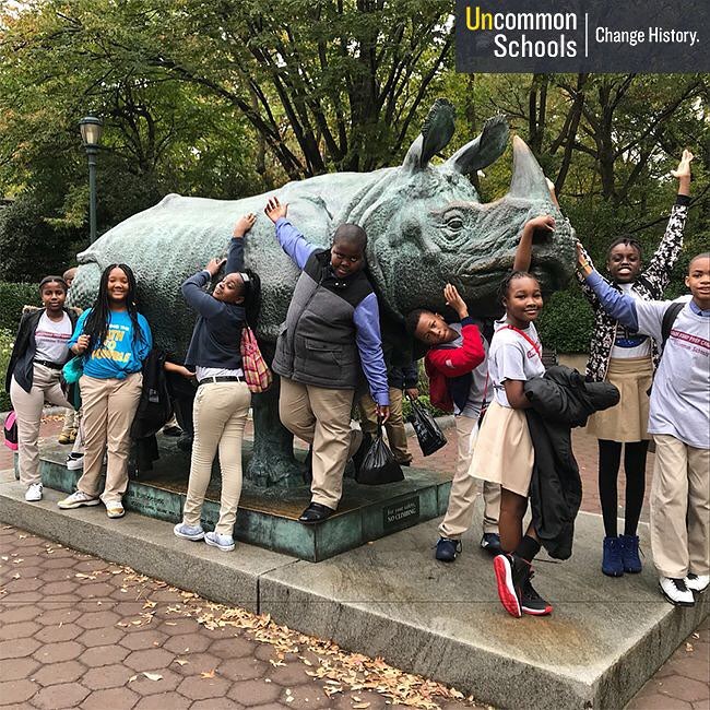 Students pose in front of a rhino statue at the Bronx Zoo