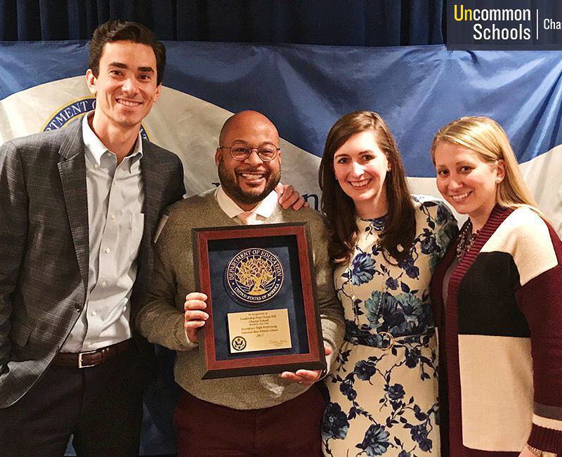 Man holds up National Blue Ribbon Award with another man and two women