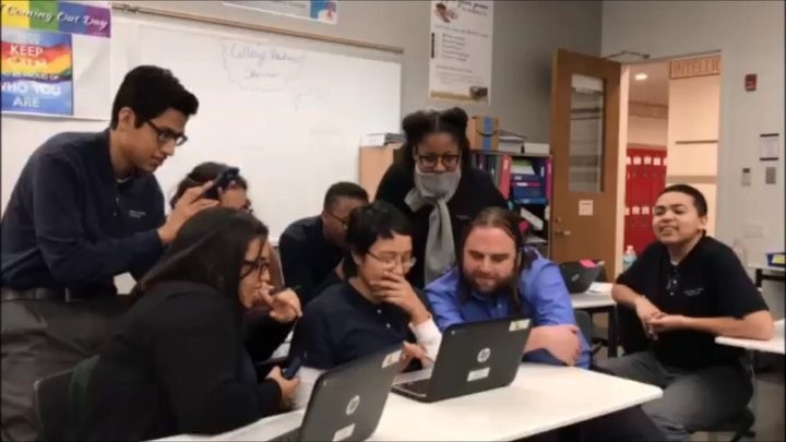 Group of students and their teacher gather behind laptops to view something