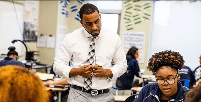 Teacher looks over a students' shoulders as they work in groups