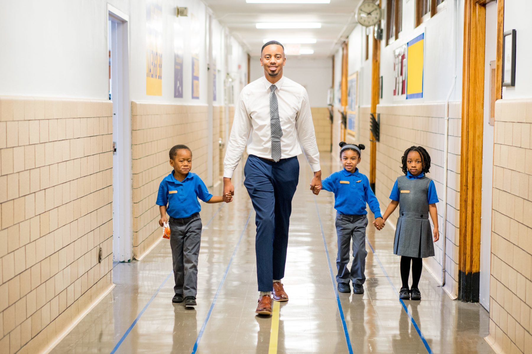 Man holding hands with young children walking down a hallway