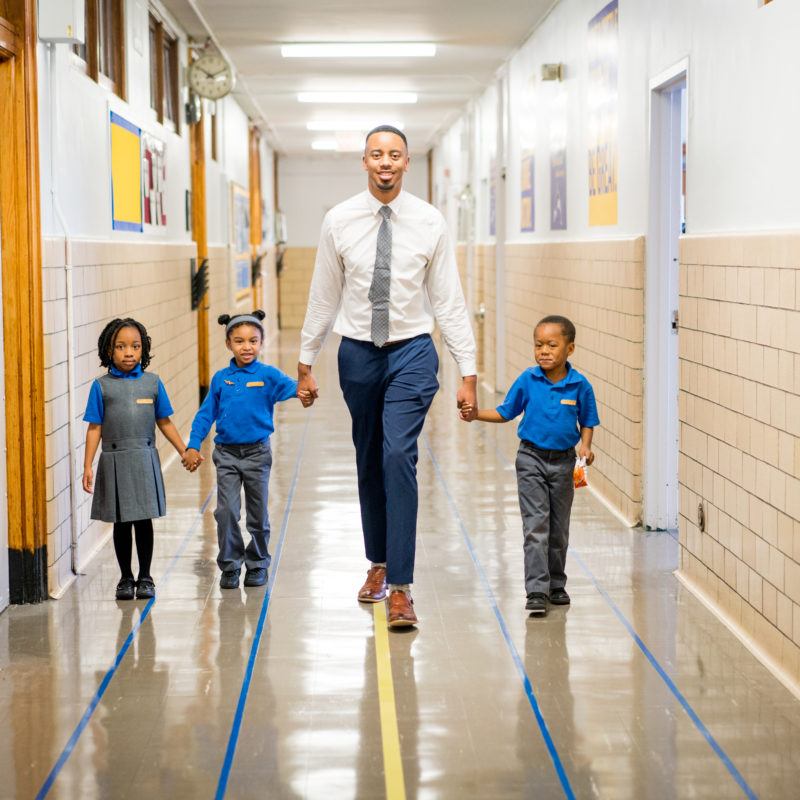 Teacher holding hands with young students in hallway