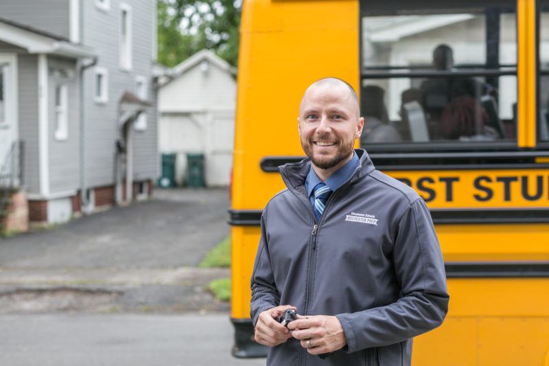 Man smiling in front of a school bus