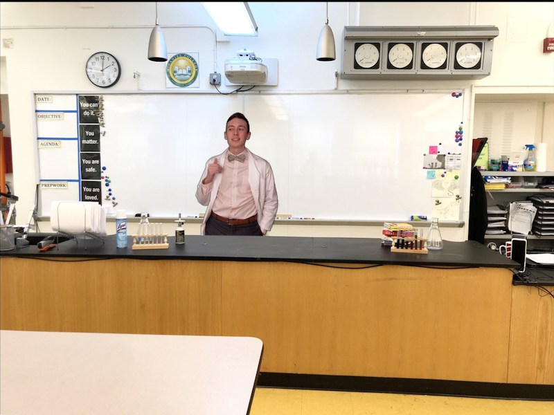 Teacher Zack Allen teaches online using a photo of his classroom lab as a backdrop.