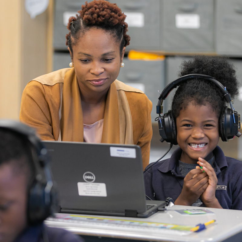Teacher helping smiling student with laptop wearing headphones