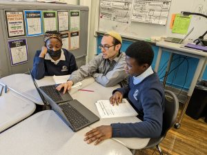 A teacher helping two students with their work on a laptop