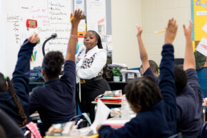 teacher in the front of the class with students raising their hands